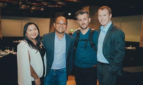 Group photo of four professionals smiling at a corporate networking event, dressed in business attire.