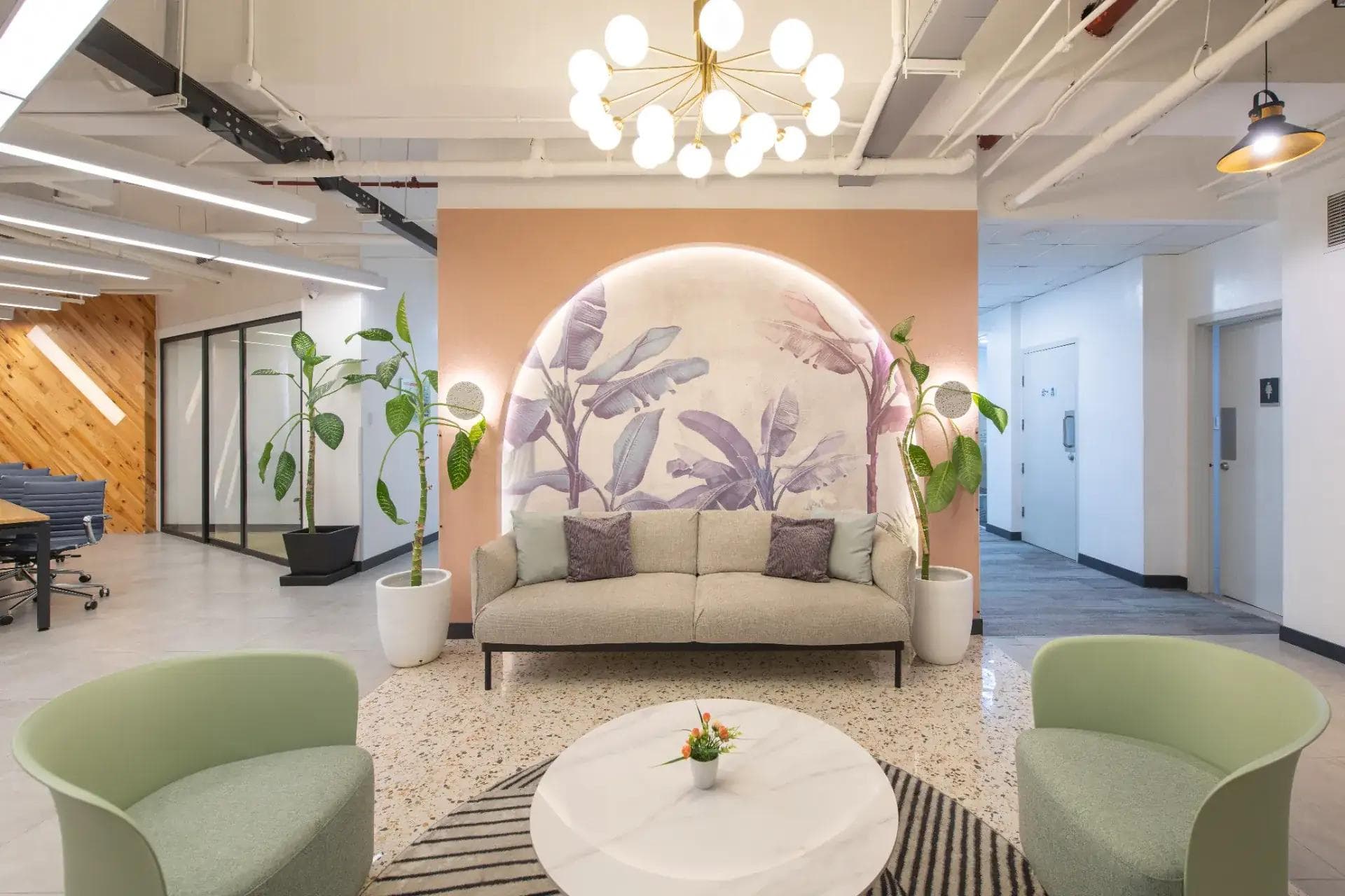 A stylish office lounge with pastel tones, cozy sofa, glass doors, ergonomic chairs, soft lighting, and plants.