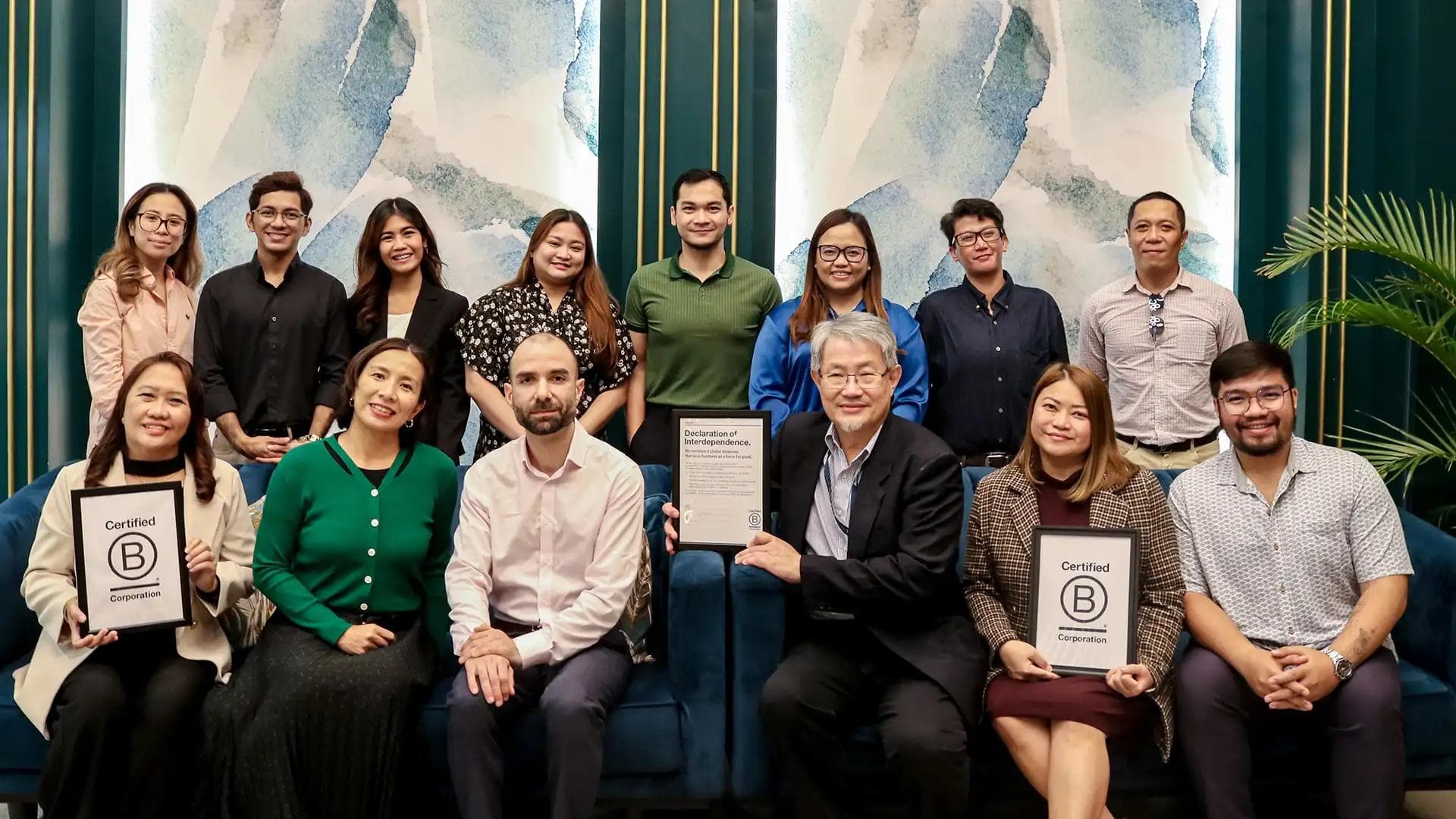 KMC's team with B Corp certification plaques, celebrating the achievement in a modern lounge with blue and green accents.