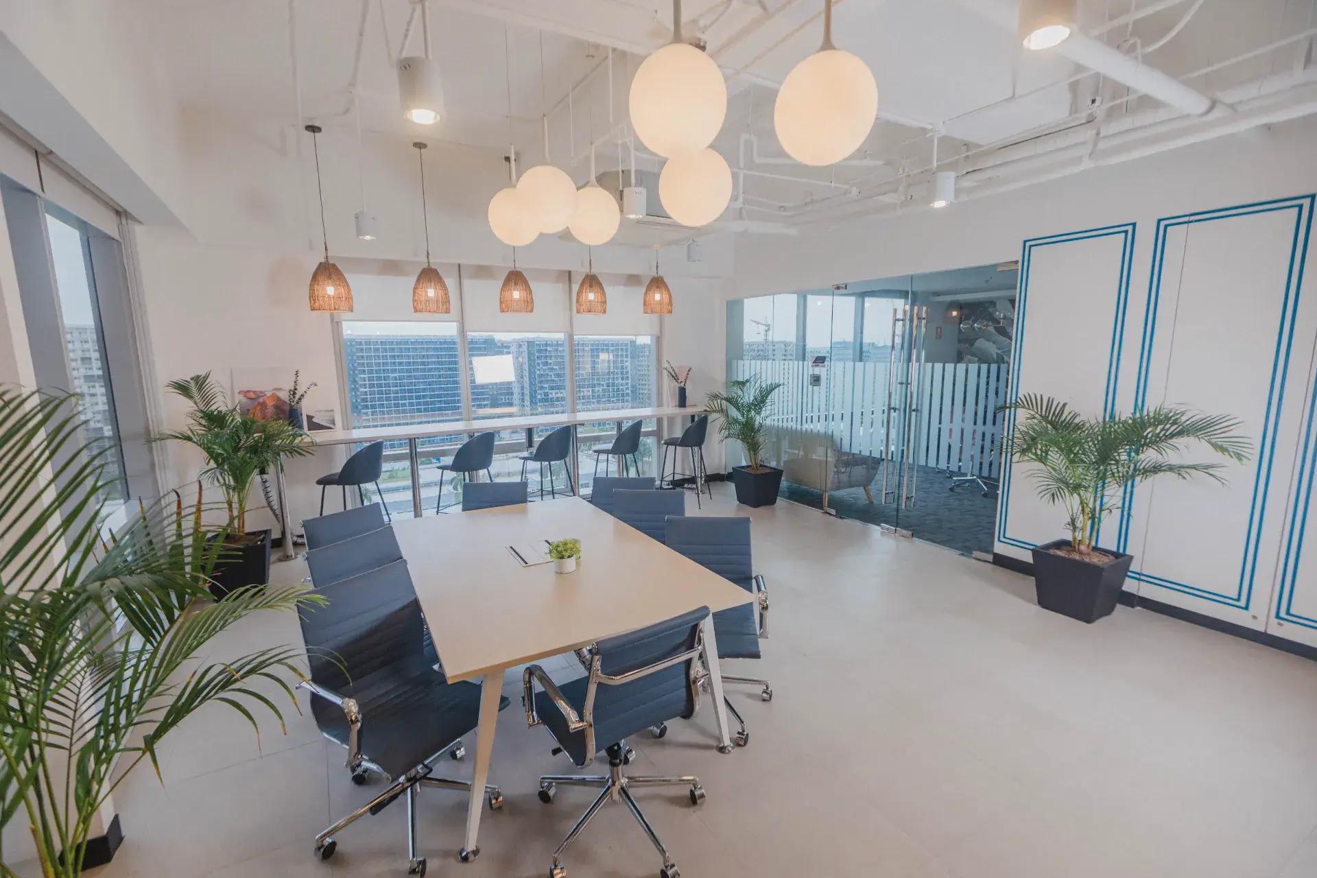 Office space in Pasay with a meeting table, bar-height seating, warm lighting, lush decor and city views in the background. Office space in Pasay with a meeting table, bar-height seating, warm lighting, lush decor and city views in the background.