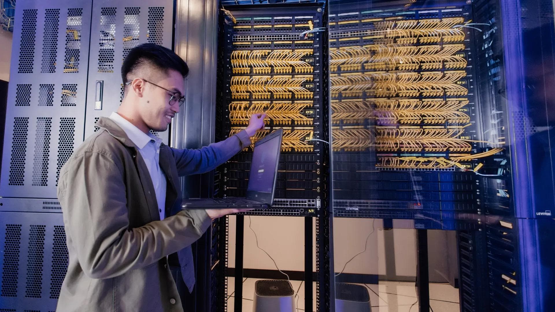 Smiling young cybersecurtiy professional working on a laptop in a modern, bright office workspace.