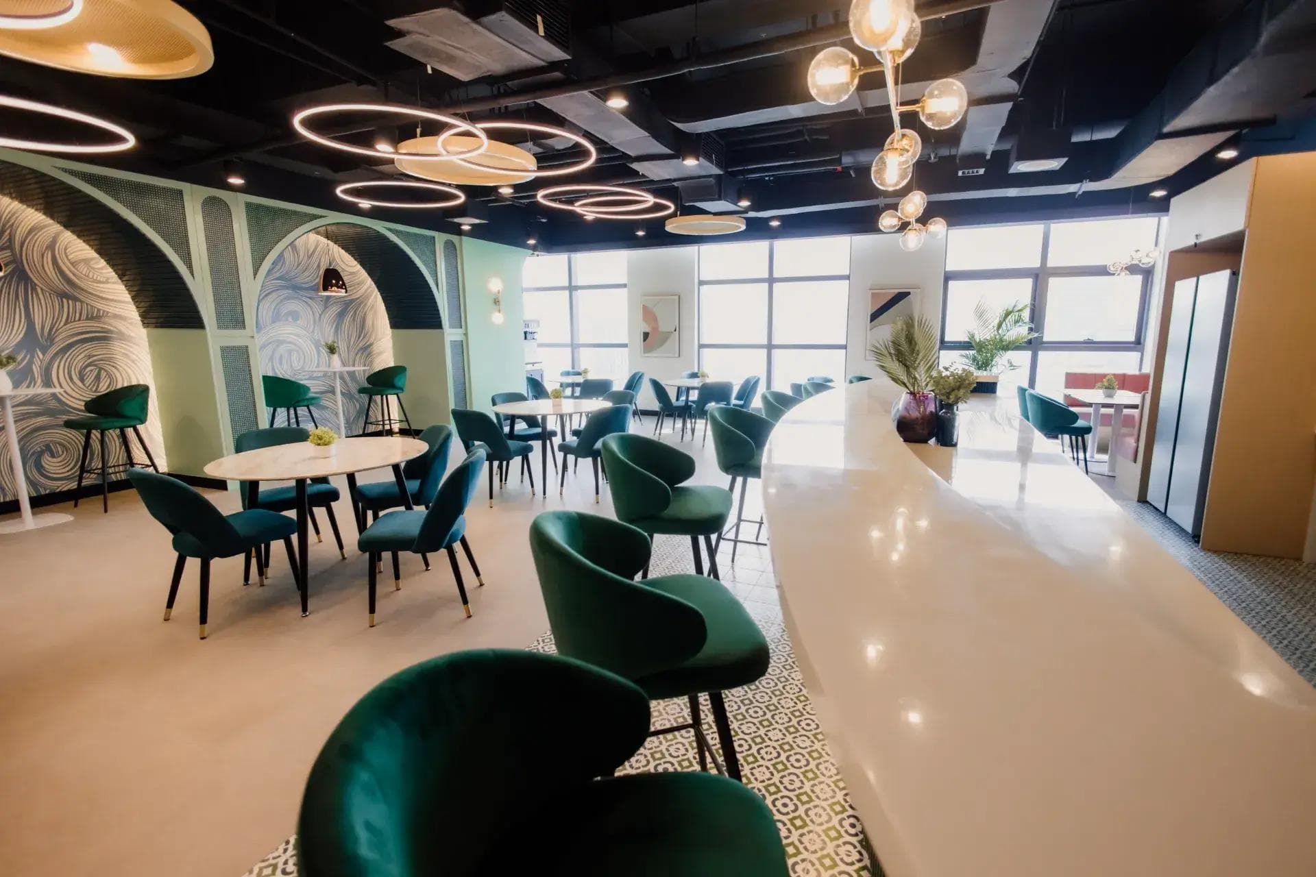KMC coworking lounge area with green velvet chairs, round tables, arch wall designs, and modern ceiling lights.
