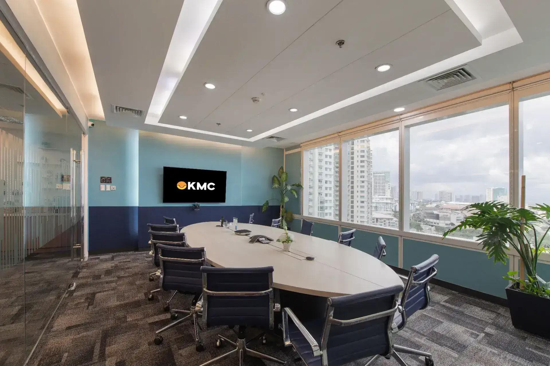 Modern Office Space in Manila with a meeting table, KMC screen, ergonomic chairs, large windows, and city skyline views.