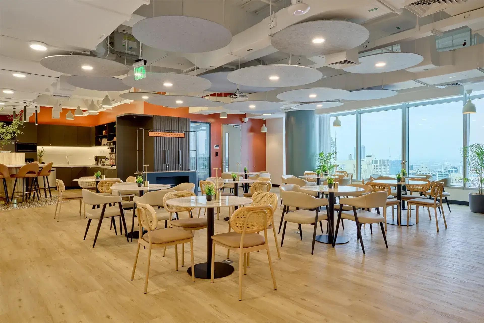 Bright café-style workspace with round tables, rattan chairs, and city views—ideal for breaks in a modern virtual office hub.