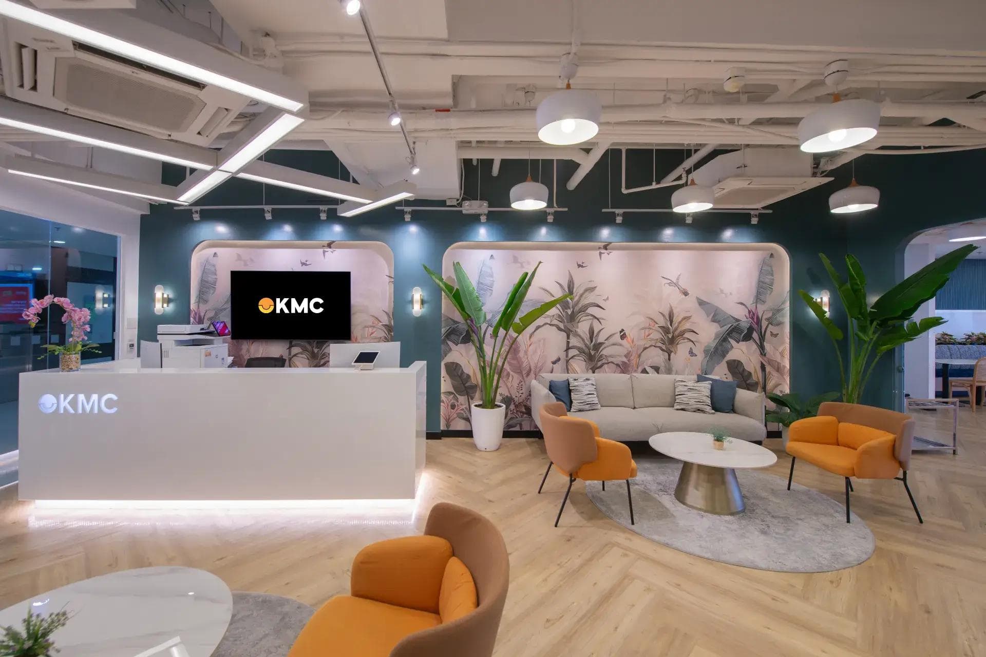 KMC reception area with modern front desk, branded signage, cozy lounge seating, and tropical wall art.