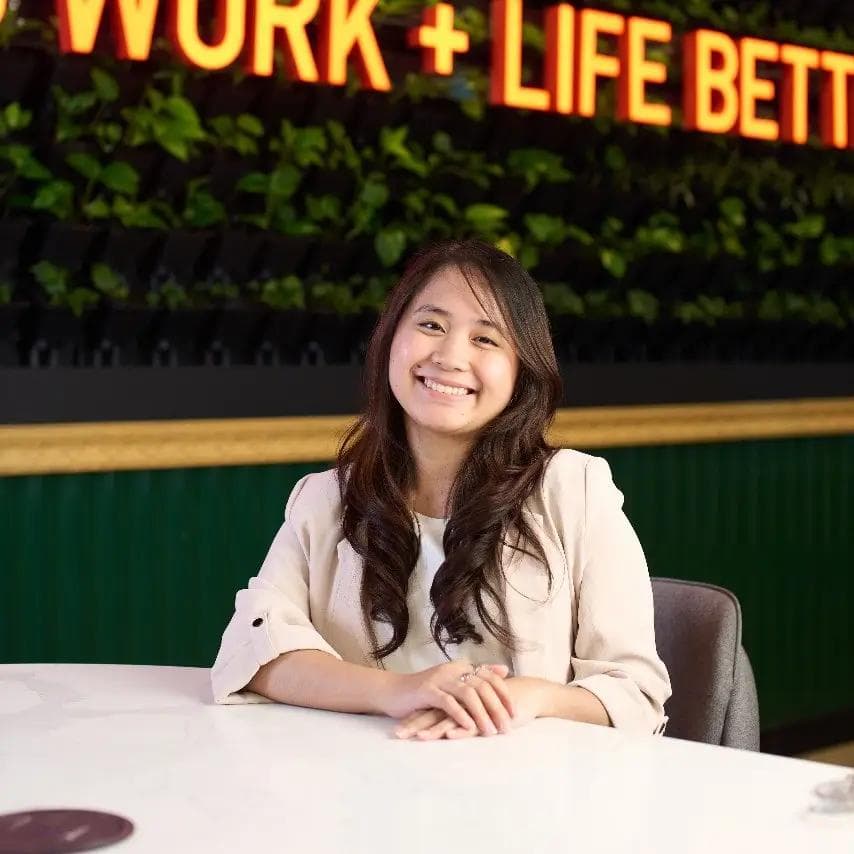 A Filipino content curator seated in a modern and well-lit Philippine office space with a “Work + Life Better” sign.