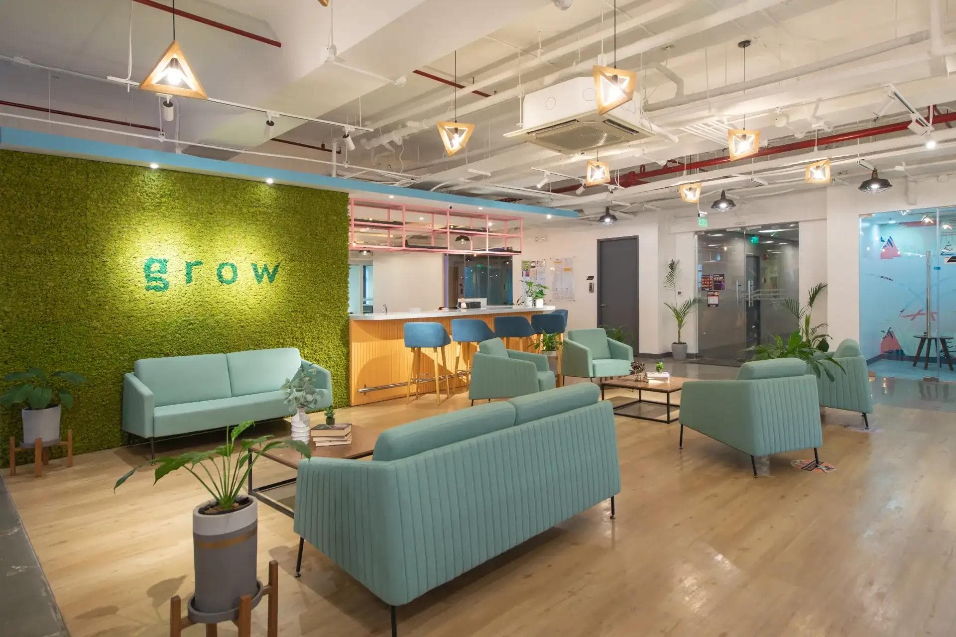 Lounge area with mint green sofas, wood flooring, and a moss wall with the word “grow” in a modern KMC coworking space.