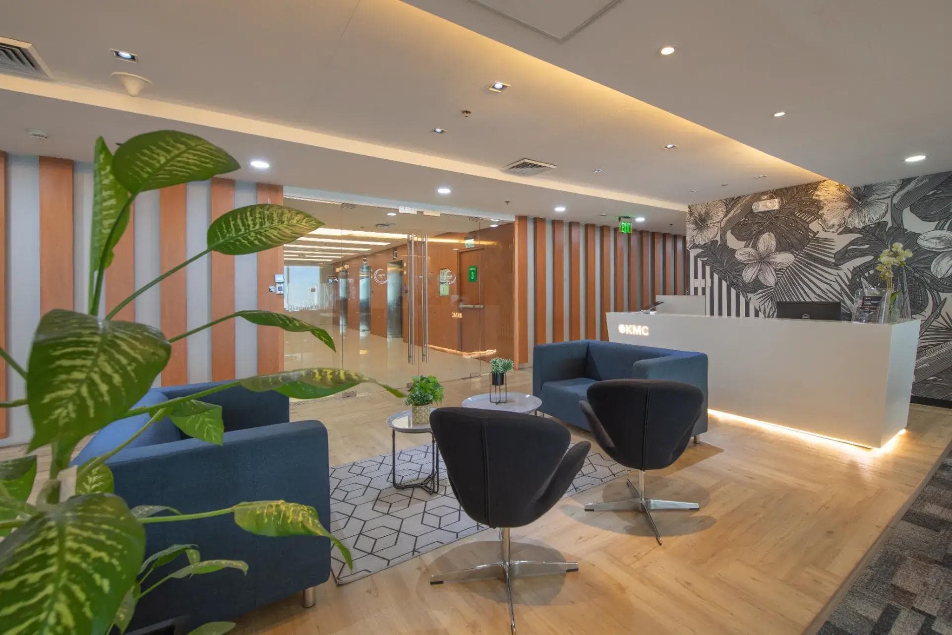Lobby with modern reception desk, striped wood walls, lounge chairs, and leafy plant decor.
