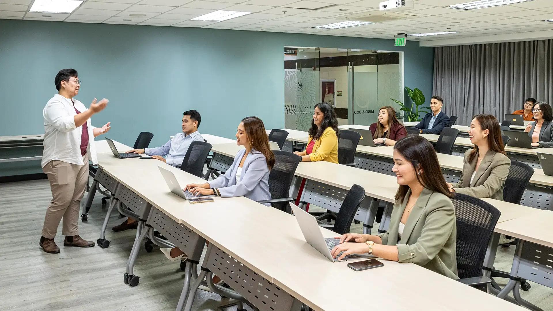 Training session in a conference room, with attendees and a speaker presenting at the front near a blue accent wall.
