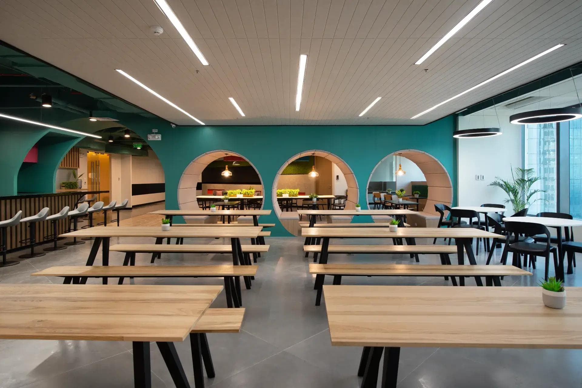 A modern coworking space with wooden tables, teal walls, and circular cutouts creating a bright, open, and collaborative vibe.