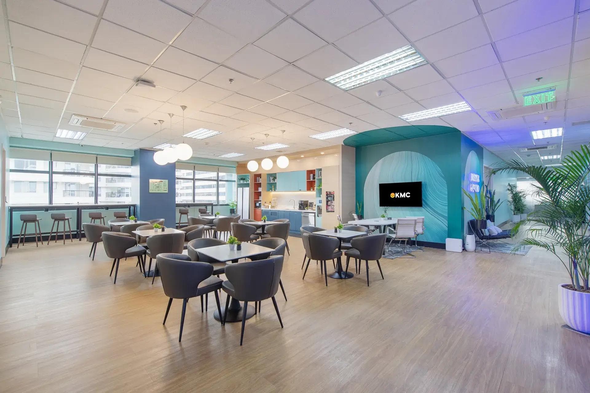 Spacious office space in HM Tower, Cebu with wood flooring, gray chairs, teal accents, indoor plants and large windows.
