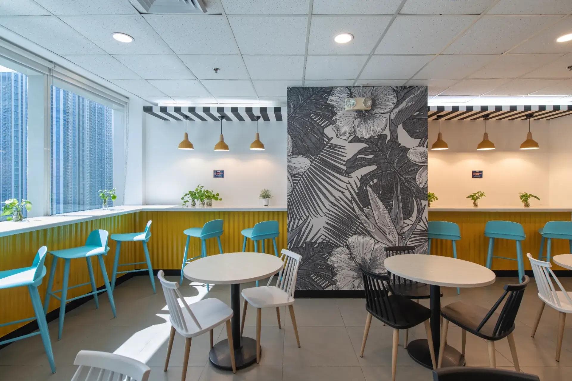 Modern coworking café with colorful bar stools, white round tables, and vibrant yellow accents, located in a KMC office space
