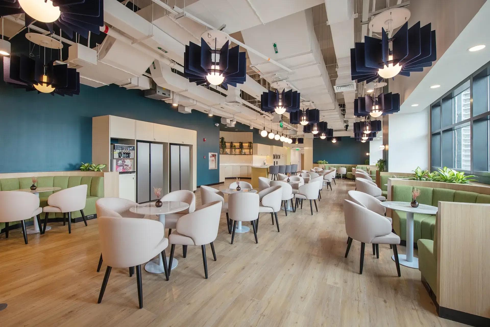 An office pantry with light wood floors, cushioned chairs, cozy booths, hanging lights, and large windows.