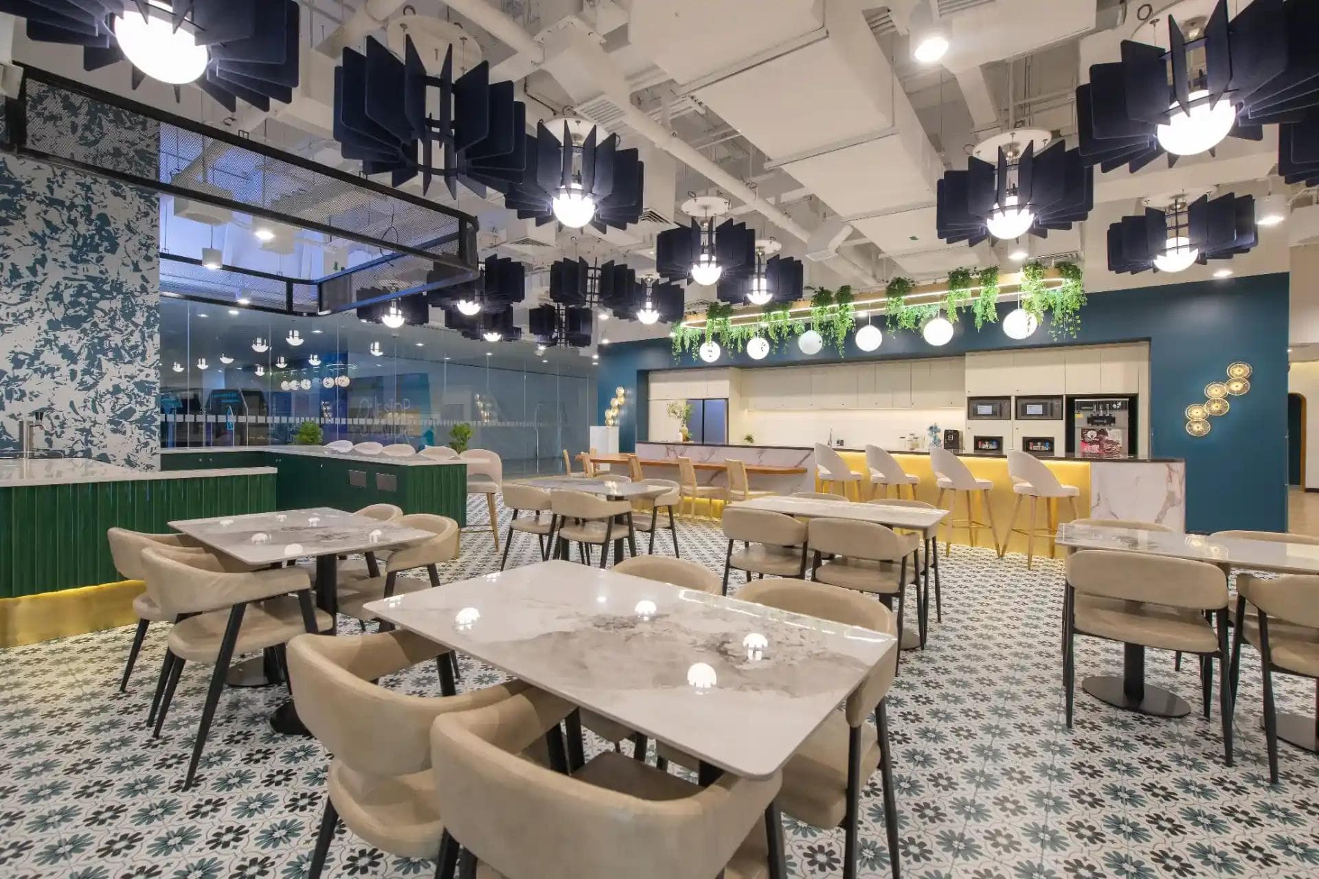 Modern coworking café with marble tables, four beige chairs, patterned tiles, globe lights, navy baffles, and a yellow bar.